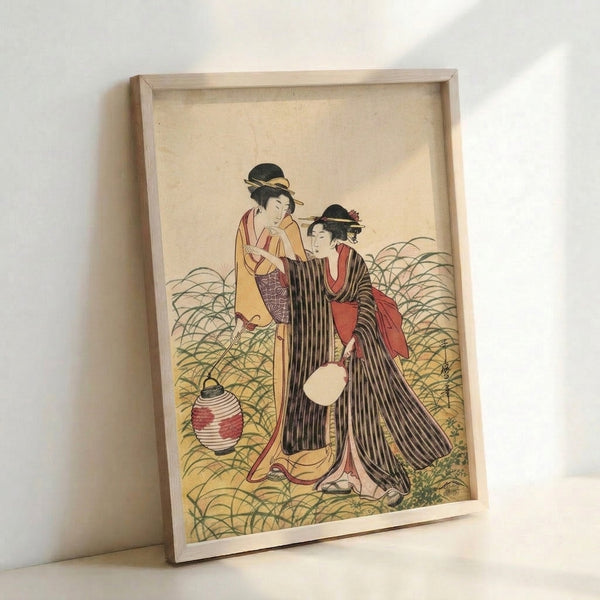 Framed art print of two poised geisha in flowing kimonos near a decorative lantern surrounded by grass, created in the serene Japanese woodblock tradition with cream, black, red, and green hues.