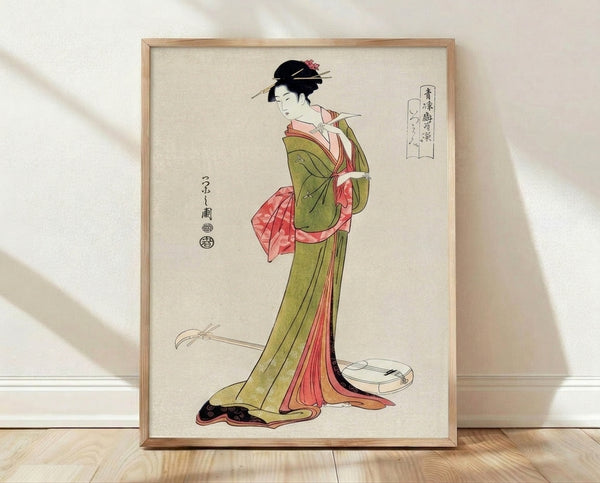 Framed Japanese woodblock print of an elegant geisha in a flowing kimono adorned with coral pink and olive green tones, holding a shamisen and wearing ornate hair accessories, rendered in traditional ukiyo-e style with gold and black accents.