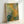 Framed garden wall art depicting flowering bushes in soft impressionist style with subtle blended hues and peaceful atmosphere.