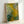 Framed botanical artwork in Impressionist style depicting a tranquil garden of white and yellow flowers amid lush green foliage and trees.