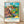 Framed Van Gogh-style impressionist landscape painting featuring a cottage nestled among trees and rolling fields under a dynamic sky in turquoise, sage green, golden yellow, and rust tones.