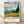 Impressionist landscape poster of a golden wheat field with tall cypress trees and rolling mountains under a dramatic, swirling sky in deep blues and creams.