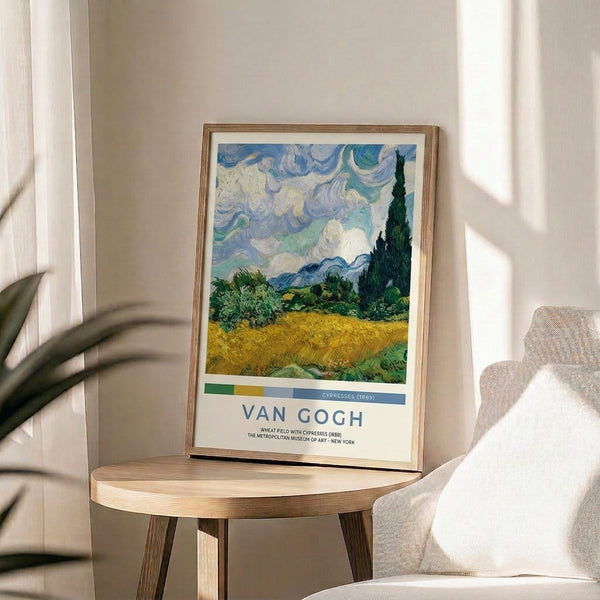 Framed impressionist landscape featuring a wheat field under stormy skies, anchored by tall cypress trees and mountains, rendered in deep blues, golden yellows, and creams.