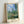 Framed art print showing Monet's contemplative view of a rural landscape with blooming poppies, tall poplar trees, and a cream-and-blue village scene.