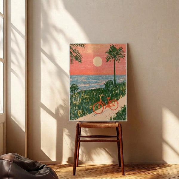 Framed wall art print in vintage aesthetic featuring a bicycle on the beach with a dramatic sunset, palm trees, and sandy dunes rendered in warm, calming coastal colors.