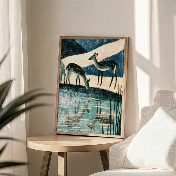 Framed mid-century style landscape art print depicting a lone deer at water's edge with mountain forest backdrop in muted cream and teal palette, evoking peaceful, contemplative atmosphere.