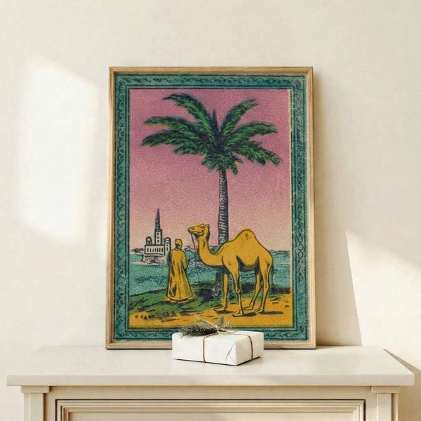 Framed matchbox-style art print depicting an oasis landscape with a camel, figure, and traditional architecture in soft cream, teal, and mauve hues.