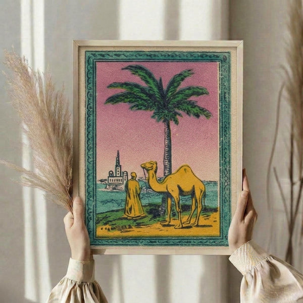 Retro-inspired travel art print featuring an oasis with camel, mosque, and palms in soft peachy, teal, and sage green; vintage matchbox label aesthetic.