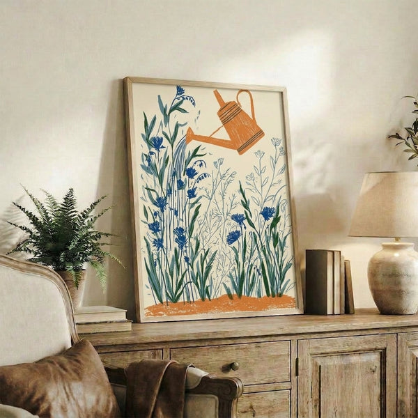 Framed wall art featuring a simple watering can with delicate cornflowers in navy and sage, inspired by vintage garden illustrations with a serene, cottagecore mood.
