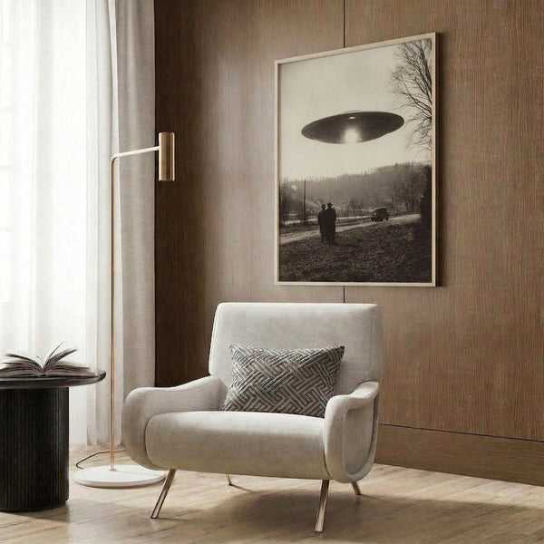 Mid-century styled artwork showing a disc-shaped spacecraft suspended over a serene rural setting with a parked car, scattered figures, and dense forest in soft sepia, gray, and cream hues creating an eerie, wondrous atmosphere.