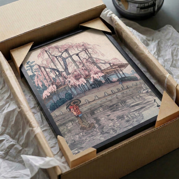 Framed East Asian woodblock art depicting a weeping willow pond garden with umbrella-holding figure, capturing melancholic tranquility through soft pink, blue-grey, and earthy brown tones.