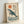 Framed art print depicting a peaceful whale swimming among gentle waves with a warm sun overhead, executed in soothing japandi colors and woodblock technique.