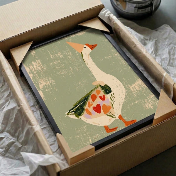Whimsical framed print of a sweet goose character sporting a heart-shaped wing among leaves and flowers, rendered in cottagecore folk art style with warm sage and rust hues.