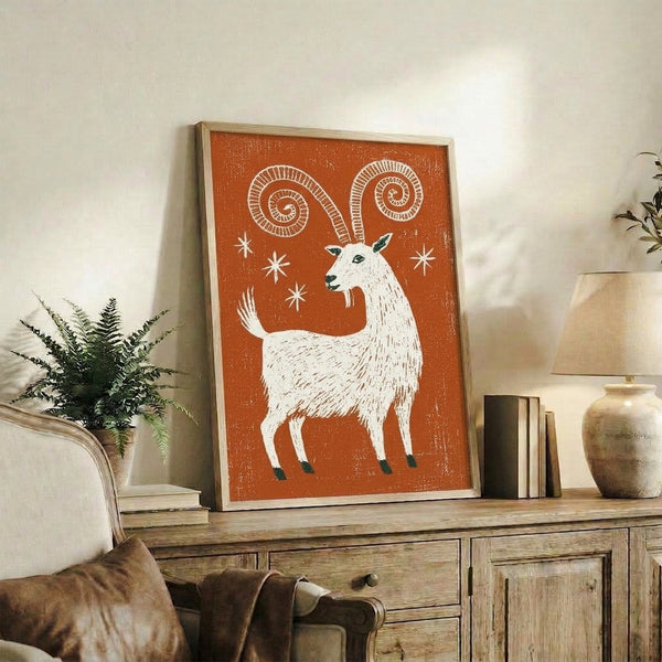 Whimsical boho-style linocut poster featuring a playful goat with curved horns surrounded by stars in warm rust and cool teal tones.