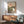 Japandi wall art depicting a solitary white cat facing a glowing sunset landscape, with sage green plants, water, and architectural elements in a serene, muted color scheme.