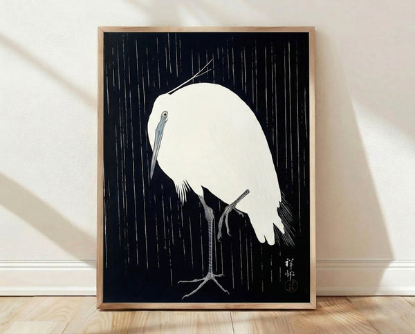 Minimalist Japanese woodblock-style framed poster depicting a crane perched on a branch in falling rain, rendered in navy and gray lines on white background.