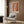 Mid-century modernist poster depicting a contemplative study of a feather and vessel in warm gold, cream, and earth-tone hues.