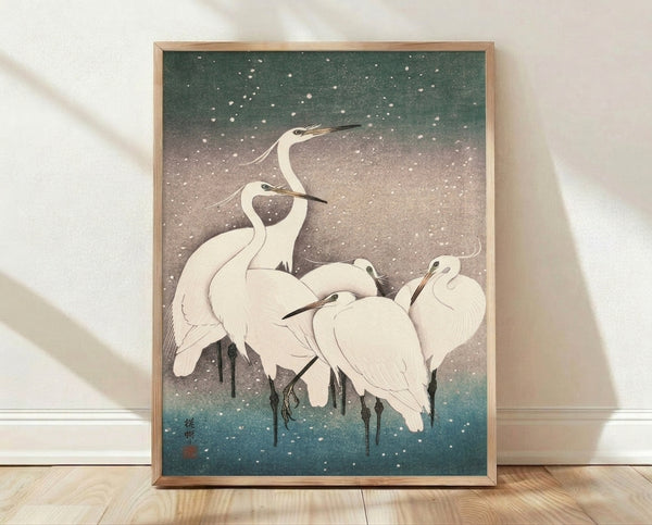 Serene Japanese woodblock print of white herons standing in snow, rendered in soft sage green, slate gray, and teal blue tones with subtle gold accents, framed as wall art.