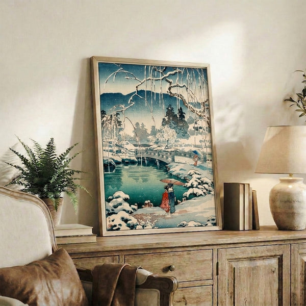 Japanese-inspired winter landscape print showing figures crossing a snow bridge beneath drooping willow branches, rendered in cool teal and cream tones.