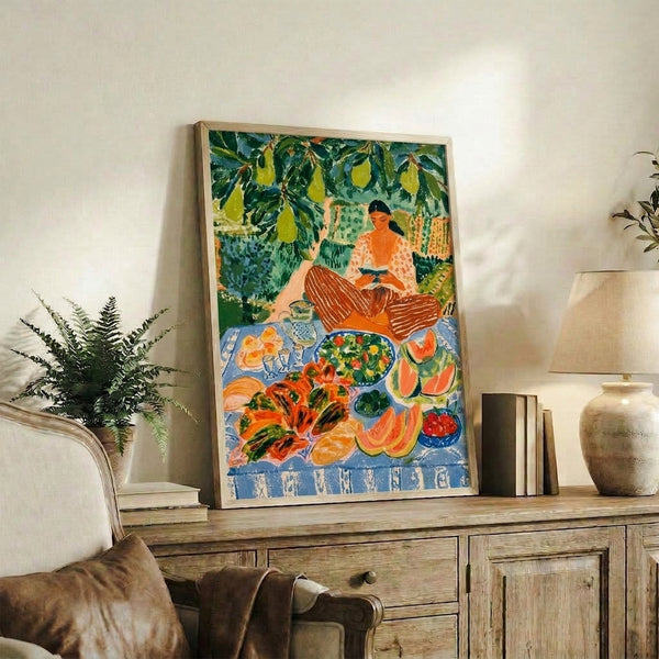 Vintage impressionist-style framed print of a peaceful woman absorbed in reading among blooming pear trees, with watermelon and salad arranged on a table, rendered in soft blues and warm greens.