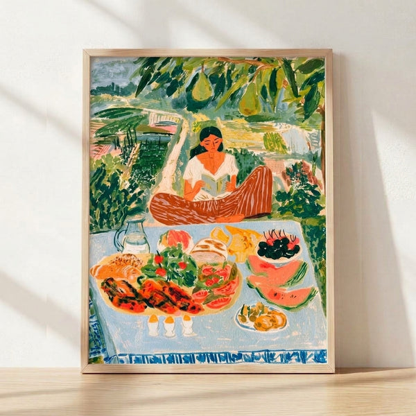 Impressionist-style framed poster depicting a woman reading a book at a garden picnic table surrounded by fresh bread, fruit, and foliage in soft sage green, terracotta, and golden yellow tones.