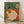 Minimalist Japandi art print of a woman in sage green interior sitting on a couch with coffee cup, plants, and books, creating a calm and cozy domestic scene in cream and terracotta tones.