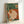 Japandi-style wall art showing an introspective woman at home with a warm beverage, comfortable couch, indoor plants, and reading materials in muted earth tones and sage green hues.