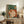 Modern minimalist art print in Japandi style portraying a cozy self-care moment with a woman, coffee cup, plants, and books in a serene sage green and burnt orange interior setting.