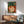 Japandi home decor poster in soft sage green and terracotta tones showing a tranquil woman enjoying coffee on a couch surrounded by botanical elements and literature.