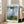 Delicate impressionist composition featuring a leisurely parasol-carrying woman in cream tones amid wildflowers and verdant landscape, suffused with tranquil sunlit atmosphere.