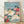 Serene Japanese woodblock print featuring a soft yellow bird perched among coral red peony blossoms and deep green leaves against a turquoise and cream background.