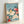 Contemplative woodblock poster showcasing a graceful yellow bird nestled beside vibrant red peony flowers with sweeping green branches on a tranquil turquoise backdrop.