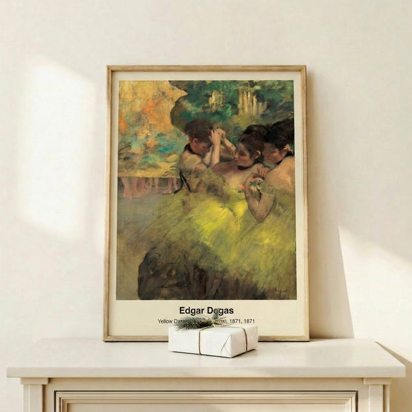 Framed mid-century inspired print of graceful ballerinas in golden yellow costumes against soft blue-toned background, in classic impressionist style.
