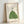 Framed poster with a hopeful, zen aesthetic featuring a child and black cat observing the night sky through a telescope on a verdant slope, rendered in sage, cream, gold, and black.